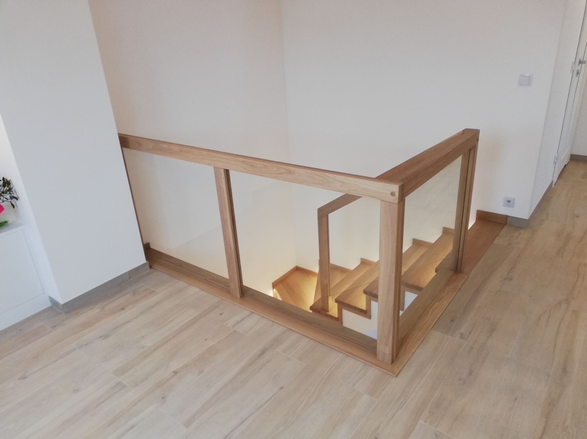 Nowoczesna balustrada szklana z drewnianymi elementami, zabezpieczająca schody. Jasne drewno i minimalistyczny design, widok z góry na fragment schodów.