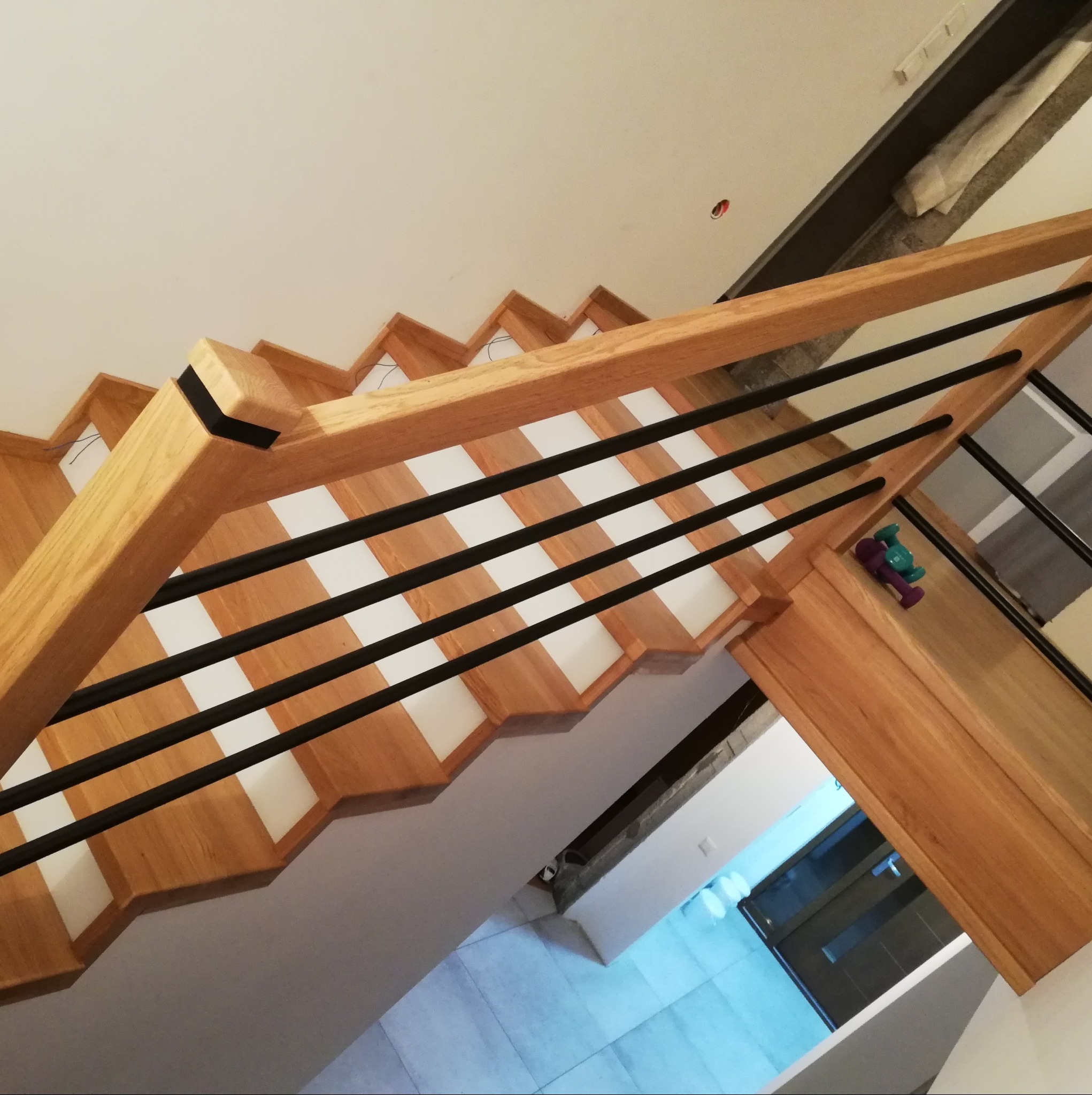 Widok z góry na jasne schody z drewnianymi stopniami i czarną balustradą. Na jednym ze stopni leżą dziecięce zabawki. Białe podstopnice tworzą kontrast.