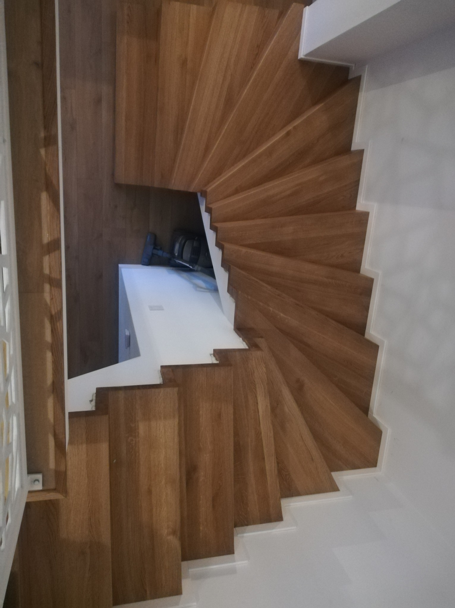 Drewniane schody spiralne z białymi podstopnicami, widok z góry. Naturalne wykończenie drewna, nowoczesny design, oświetlenie naturalne.