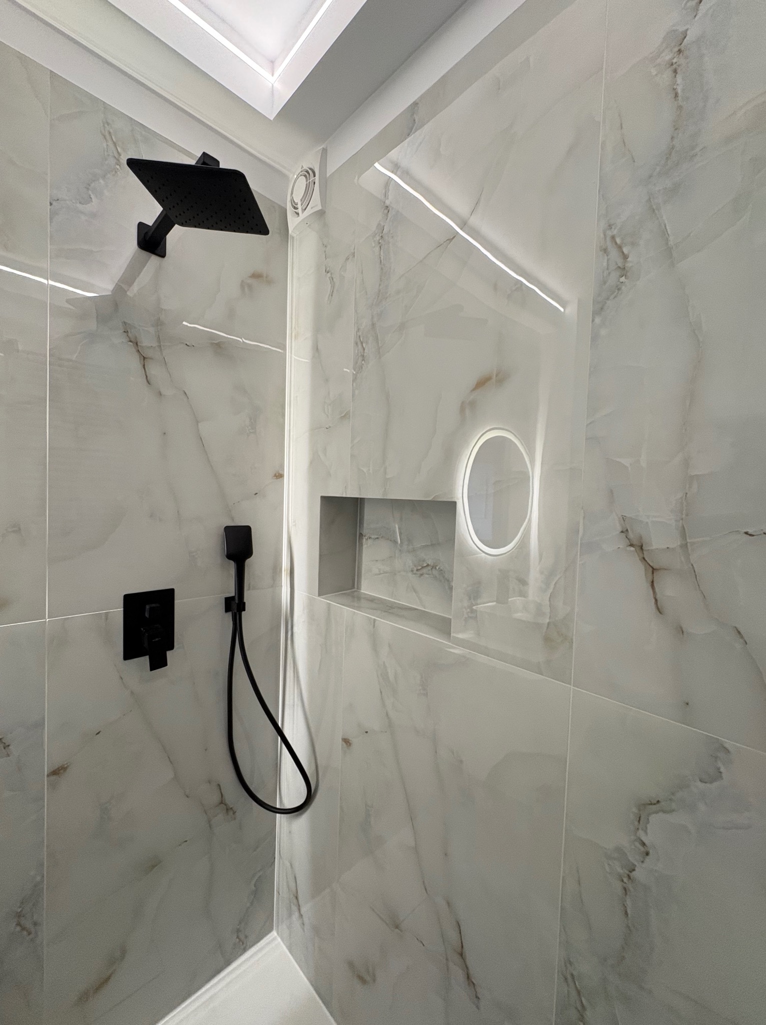 Wykończona łazienka z marmurowymi płytkami, czarną armaturą i podświetlaną wnęką. Nowoczesny design z dbałością o detale.