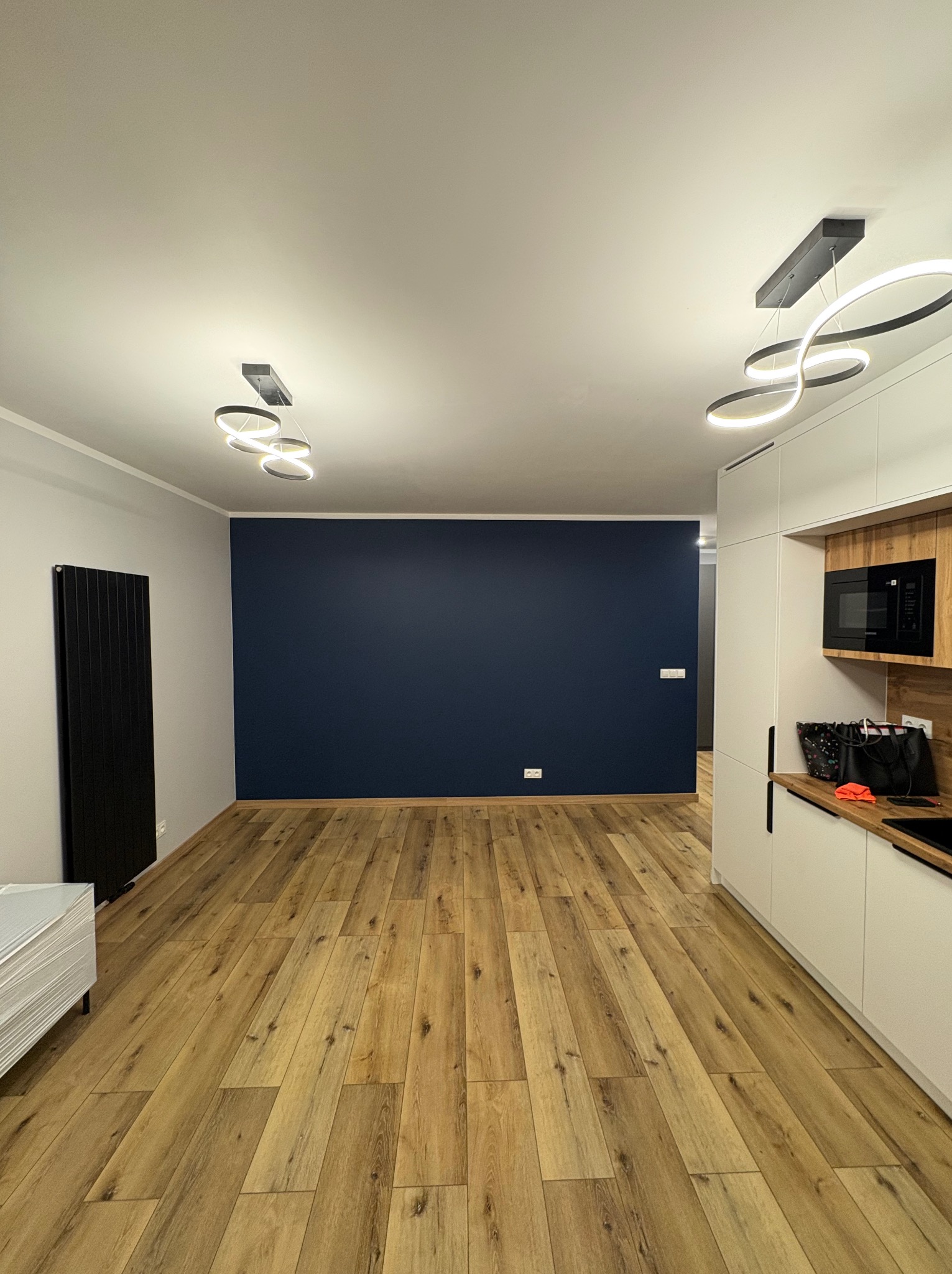 Nowoczesne wnętrze: drewniana podłoga, granatowa ściana, białe meble kuchenne z drewnianymi akcentami i designerskie lampy sufitowe.