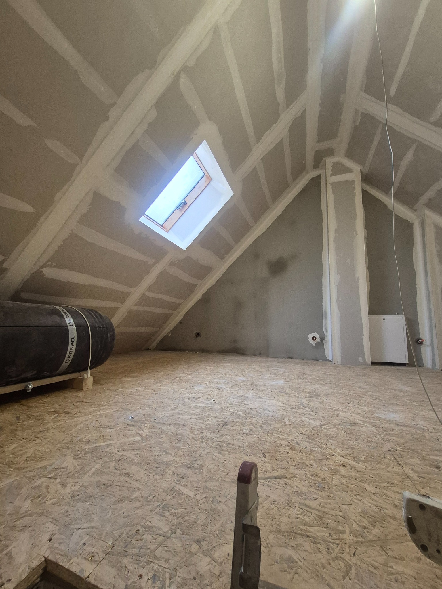 Poddasze w trakcie adaptacji: płyty gipsowe zamontowane na skosach i suficie, widoczne łączenia płyt przygotowane do szpachlowania. Na podłodze płyta OSB.