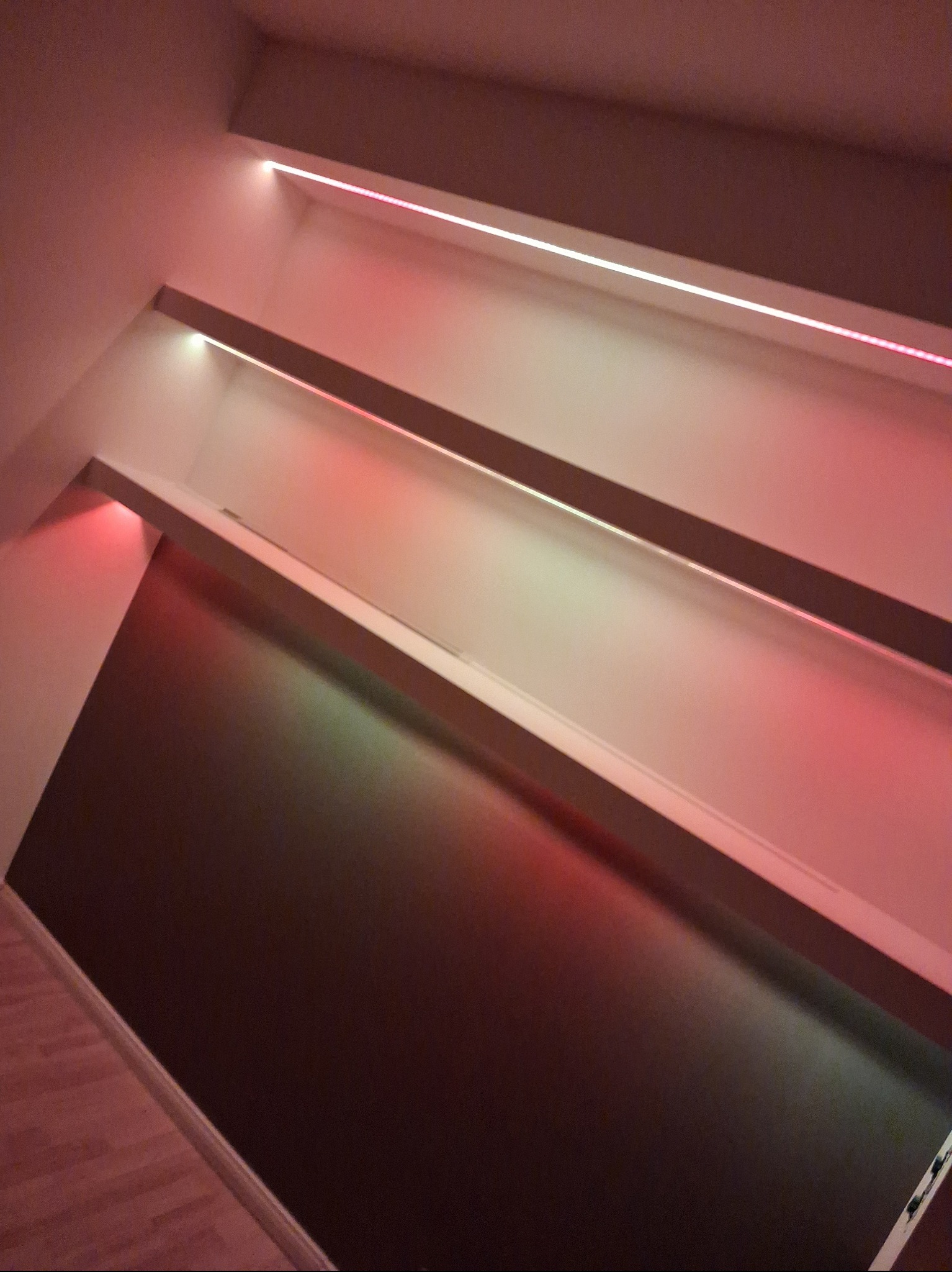 Ciemnobrązowa ściana z trzema poziomami podświetlanych półek, oświetlonych ciepłym, czerwonym światłem LED, tworzących nowoczesny, minimalistyczny design wnętrza.