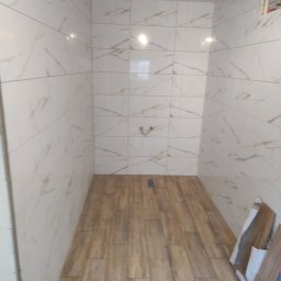 Modern House Mateusz Kuras - Wykończona łazienka z drewnopodobną podłogą i marmurowymi płytkami na ścianach. Widoczne fragmenty płytek przy ścianie. Minimalistyczny design.