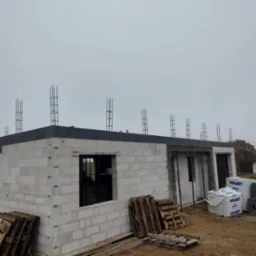 Wznoszenie ścian z bloczków betonu komórkowego na budowie domu. Widoczne zbrojenia pionowe, palety i materiały budowlane Solbet.