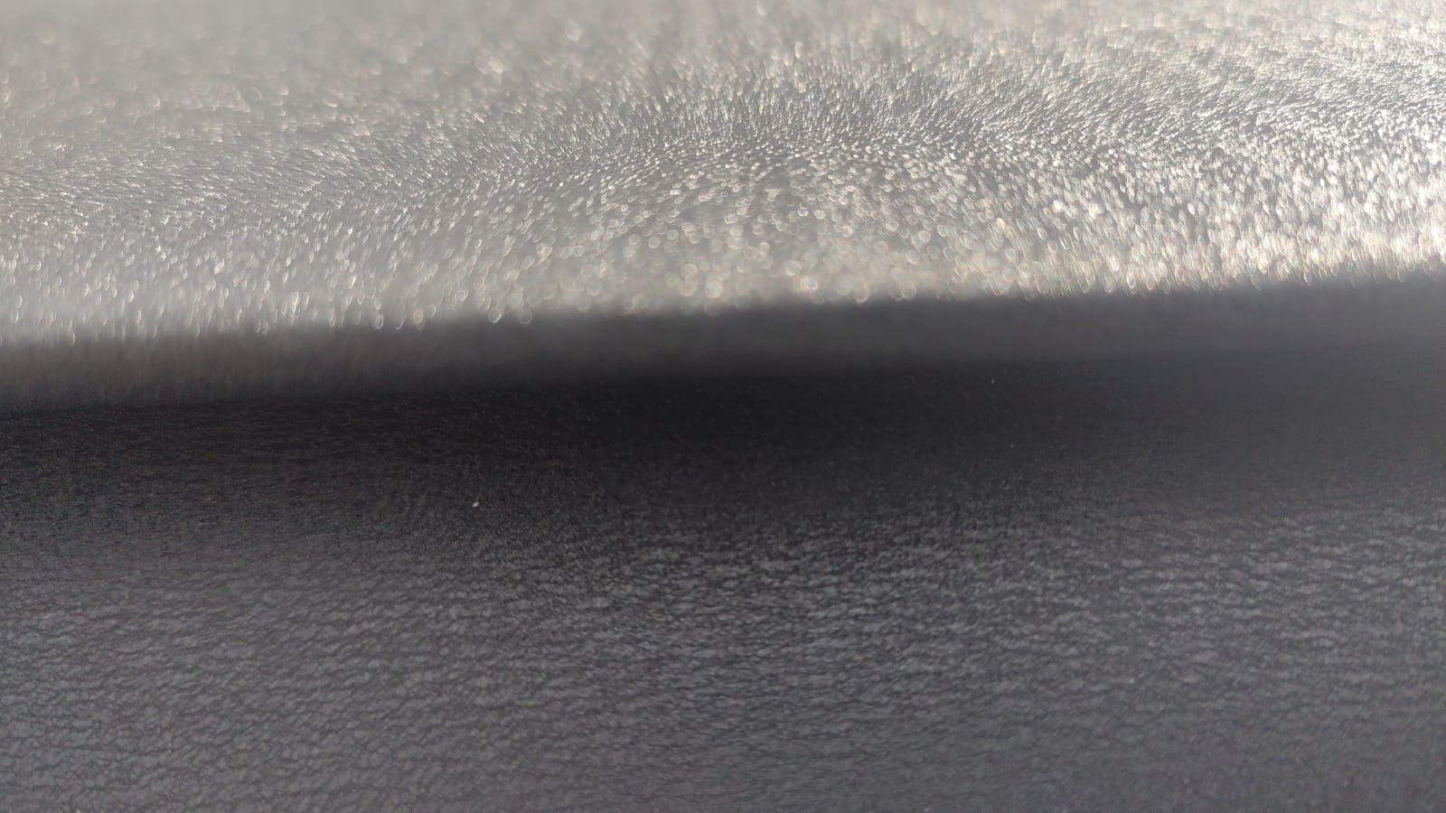 Zbliżenie na czarną, teksturowaną powierzchnię z refleksami światła, tworzącą abstrakcyjny, minimalistyczny obraz.