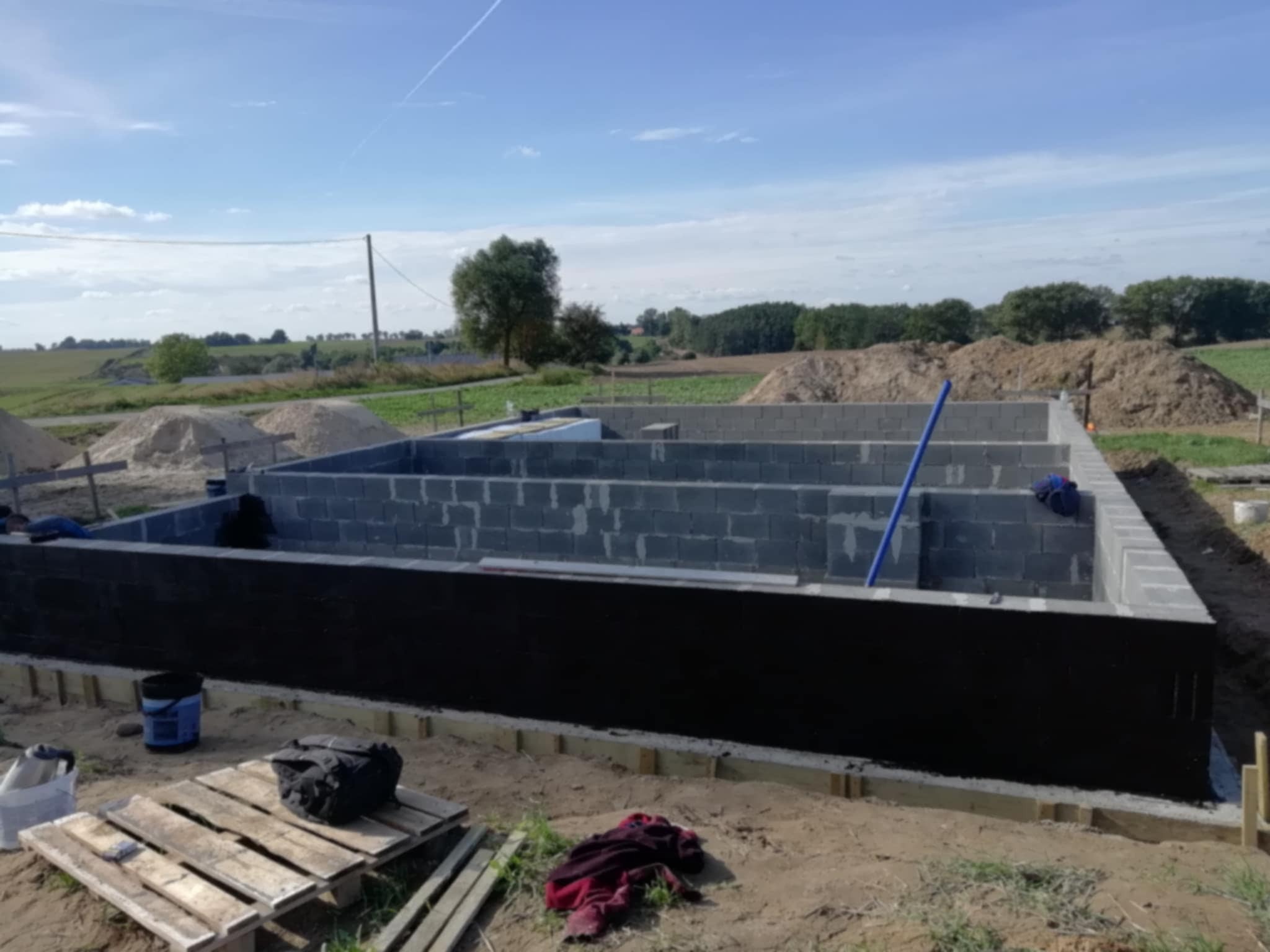 Fundamenty z bloczków betonowych, zabezpieczone izolacją przeciwwilgociową, widoczne narzędzia i materiały budowlane na placu budowy.