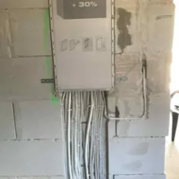 Montaż rozdzielnicy Volta z licznymi kablami w ścianie z betonu komórkowego, widoczne mocowania i schematy na obudowie. Instalacja elektryczna w trakcie prac.