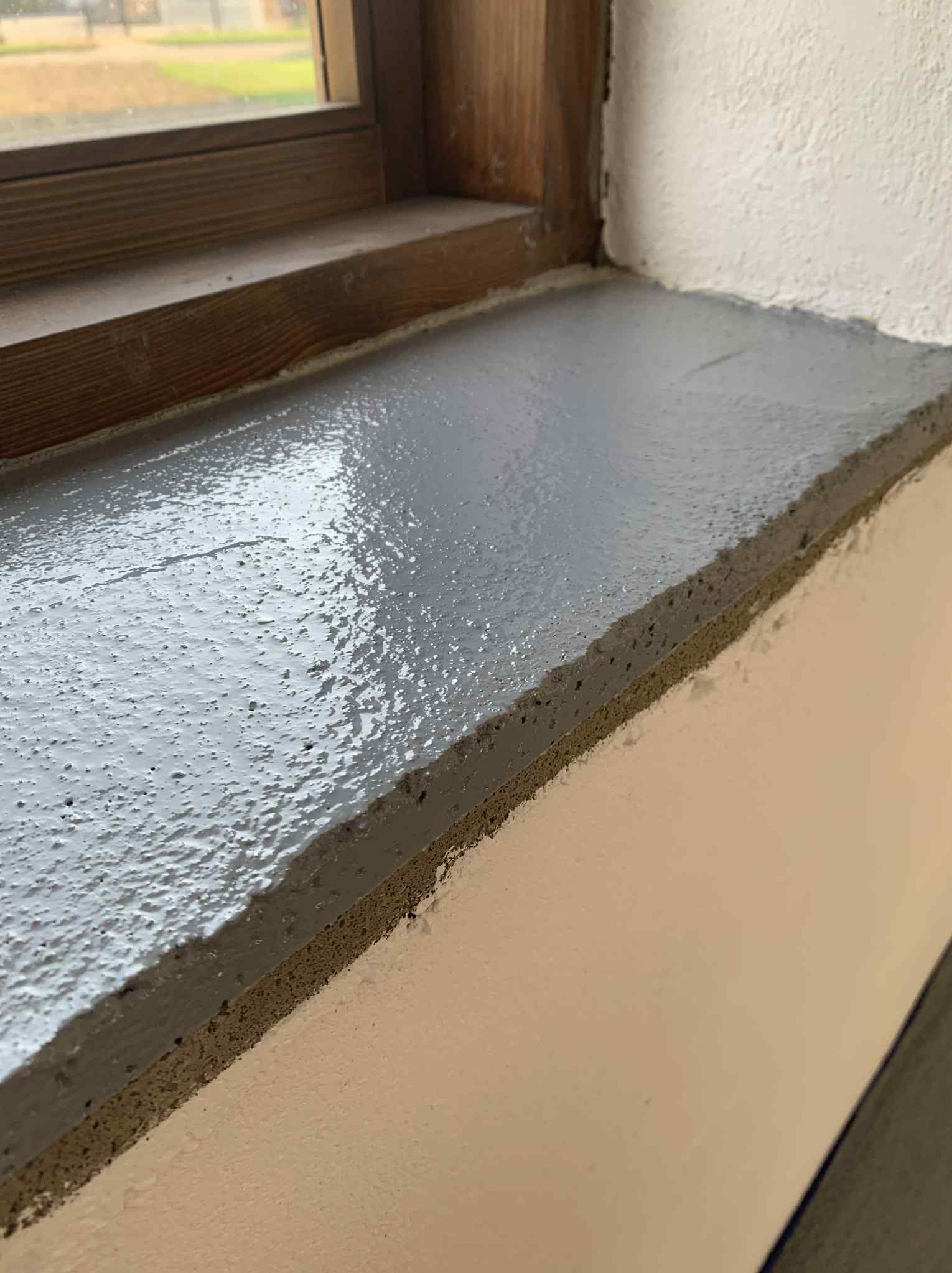 Świeżo pomalowany, szary parapet okienny z drewnianą ramą, widoczny z bliska, z fakturą farby i tłem w postaci białej ściany.