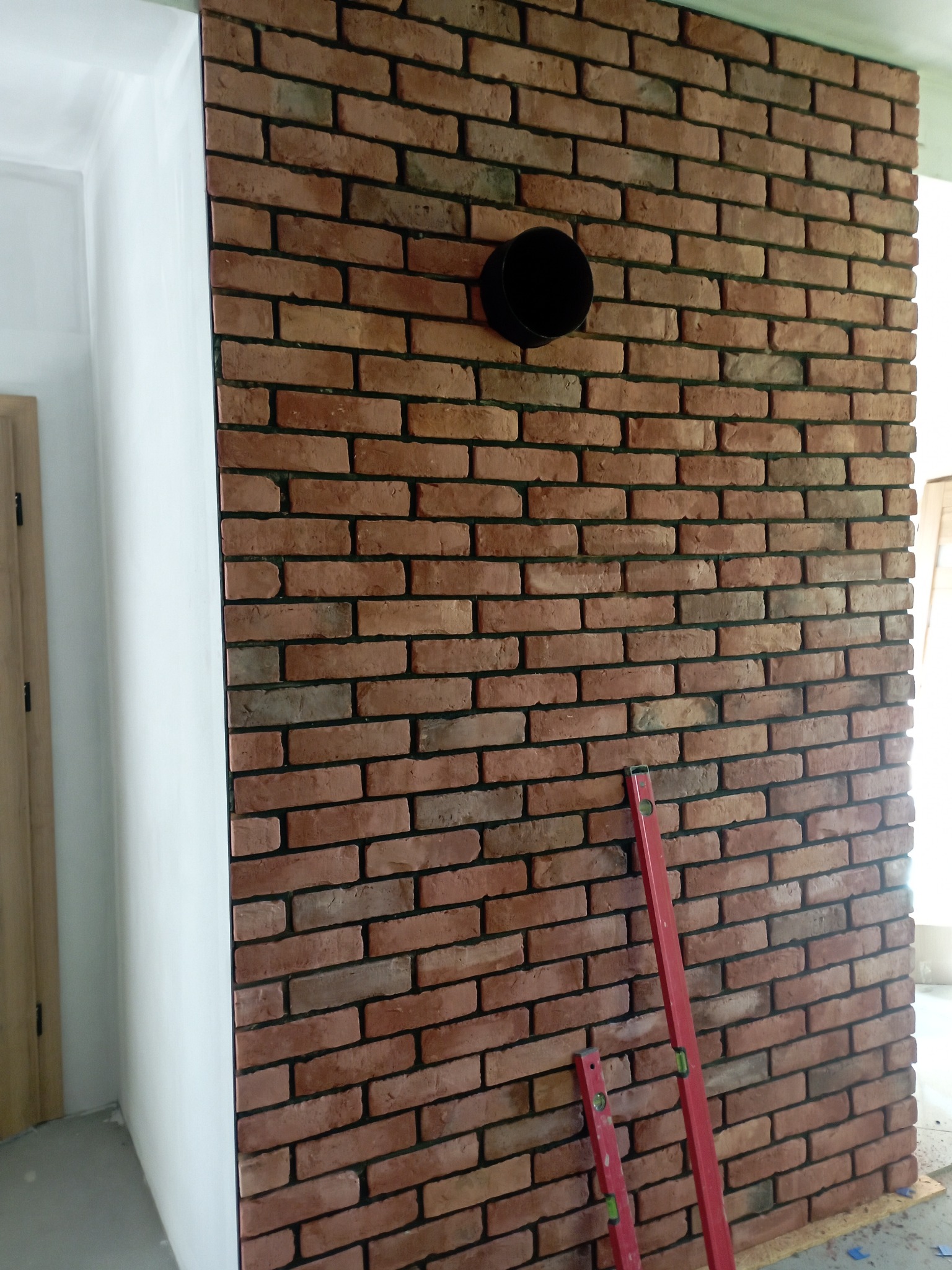 Ściana z cegły klinkierowej z otworem wentylacyjnym, częściowo przylegająca do białej ściany. Poziomice murarskie oparte o cegły. Wykończenie wnętrz.