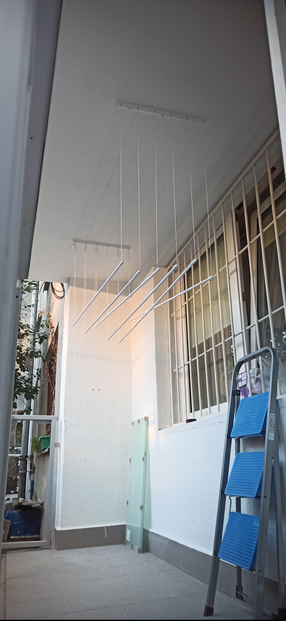 Biały balkon po odświeżeniu z rozwieszoną suszarką sufitową, drabina oparta o ścianę, widok z dołu. Świeżo pomalowane ściany i sufit.