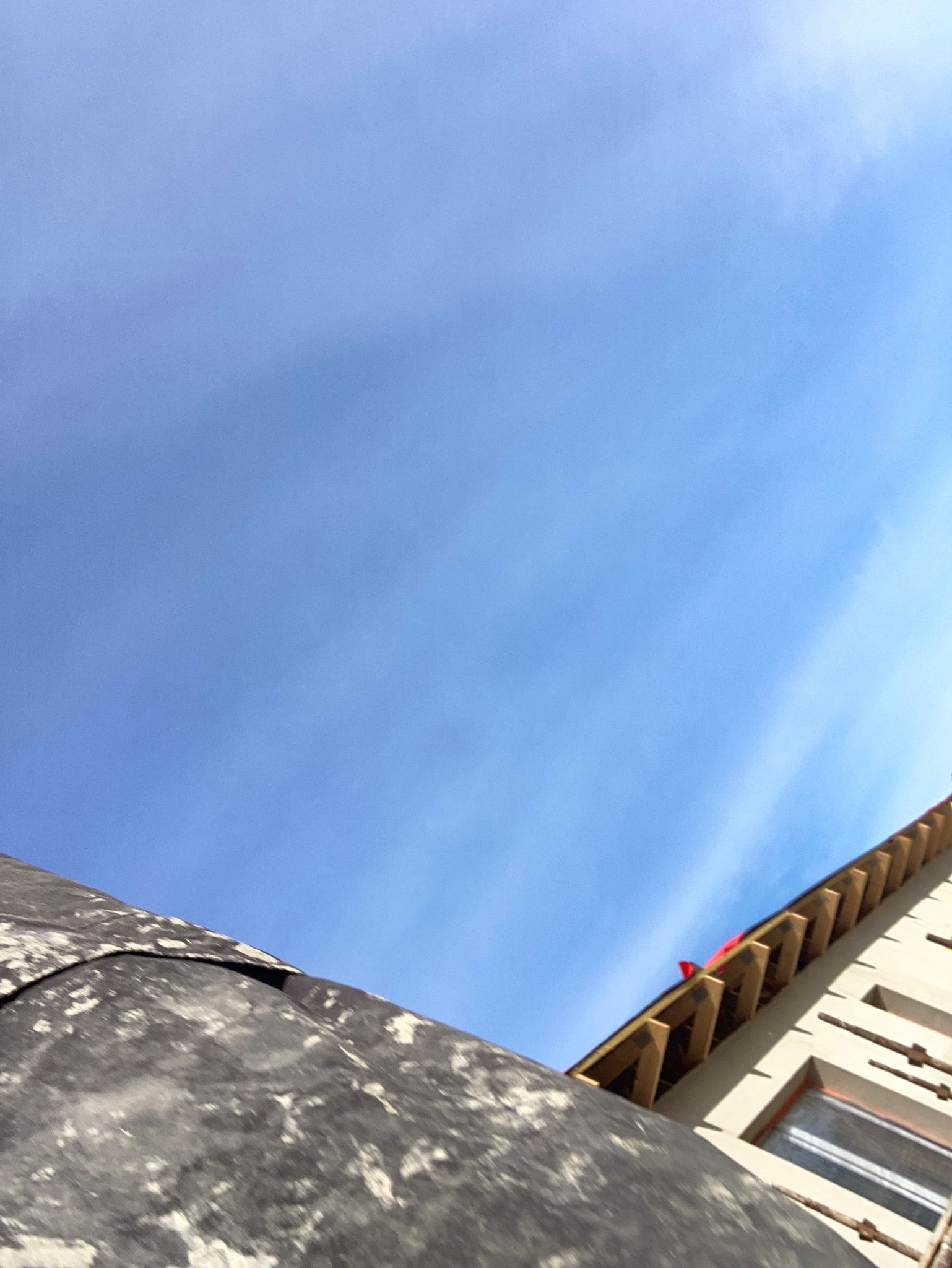 Nietypowy kadr: fragment elewacji budynku w trakcie prac wykończeniowych, widok z dołu na tle błękitnego nieba. Widoczne rusztowania i surowe drewno konstrukcji.