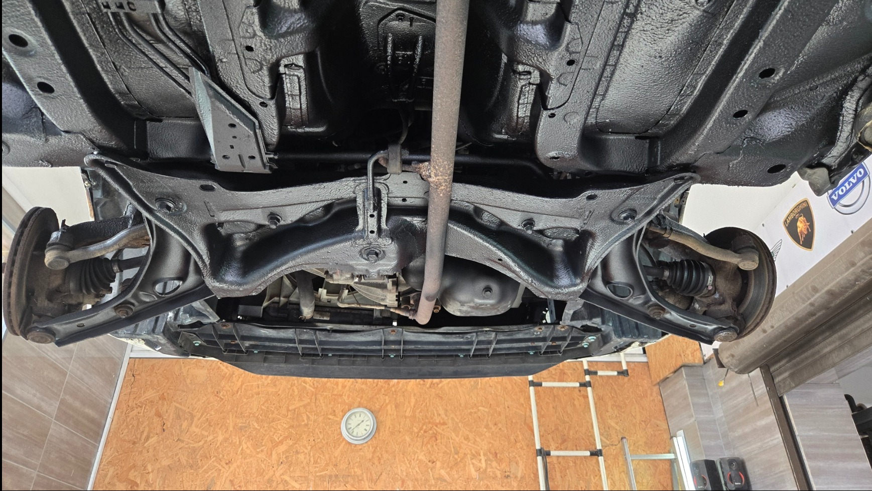 Podwozie samochodu po zabezpieczeniu antykorozyjnym, widoczne elementy zawieszenia i układu wydechowego. Świeża, czarna powłoka ochronna na metalowych elementach.