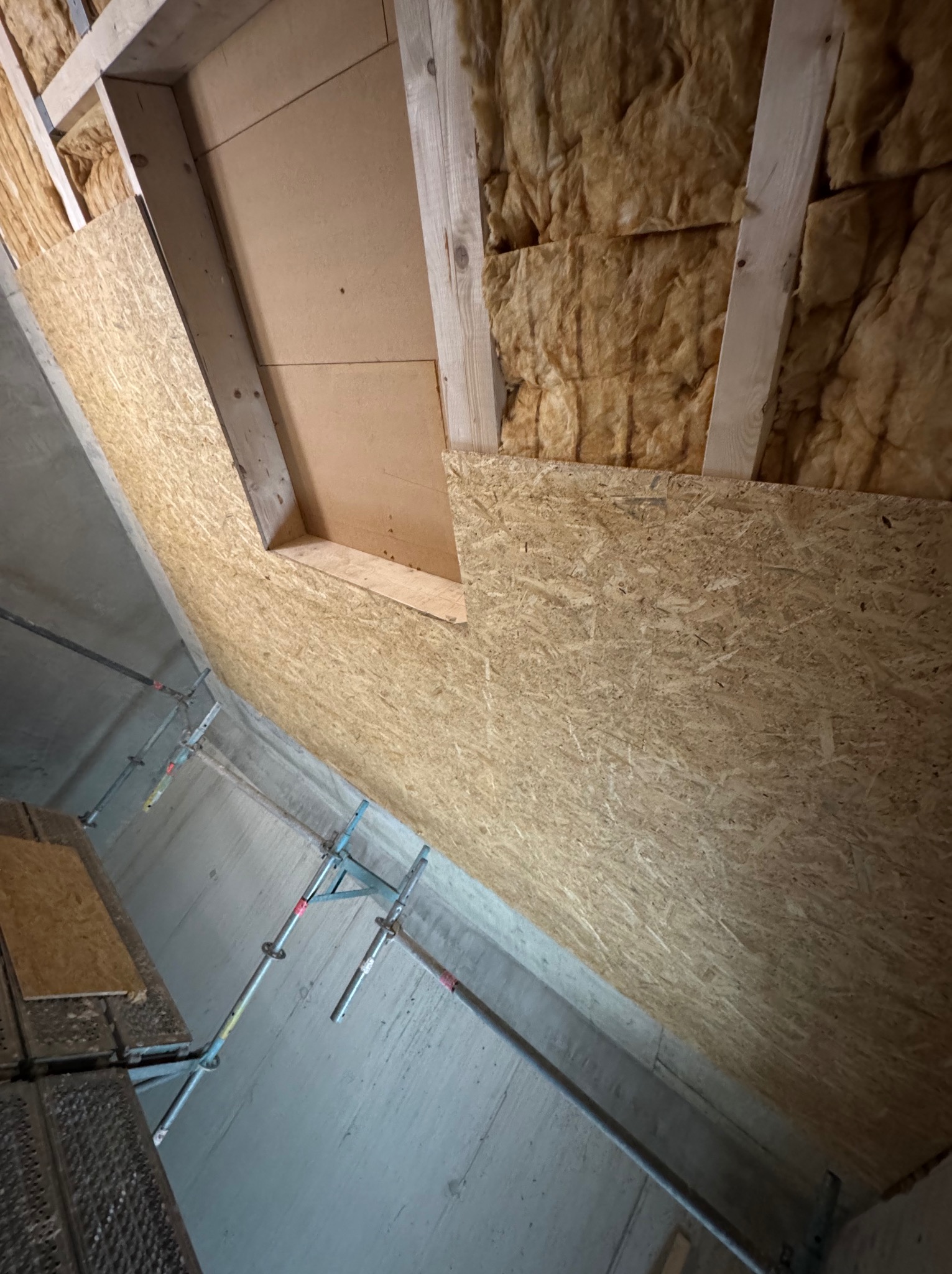 Ocieplenie poddasza wełną mineralną, obłożone płytą OSB. Widoczne rusztowanie. Prace wykończeniowe w trakcie realizacji.