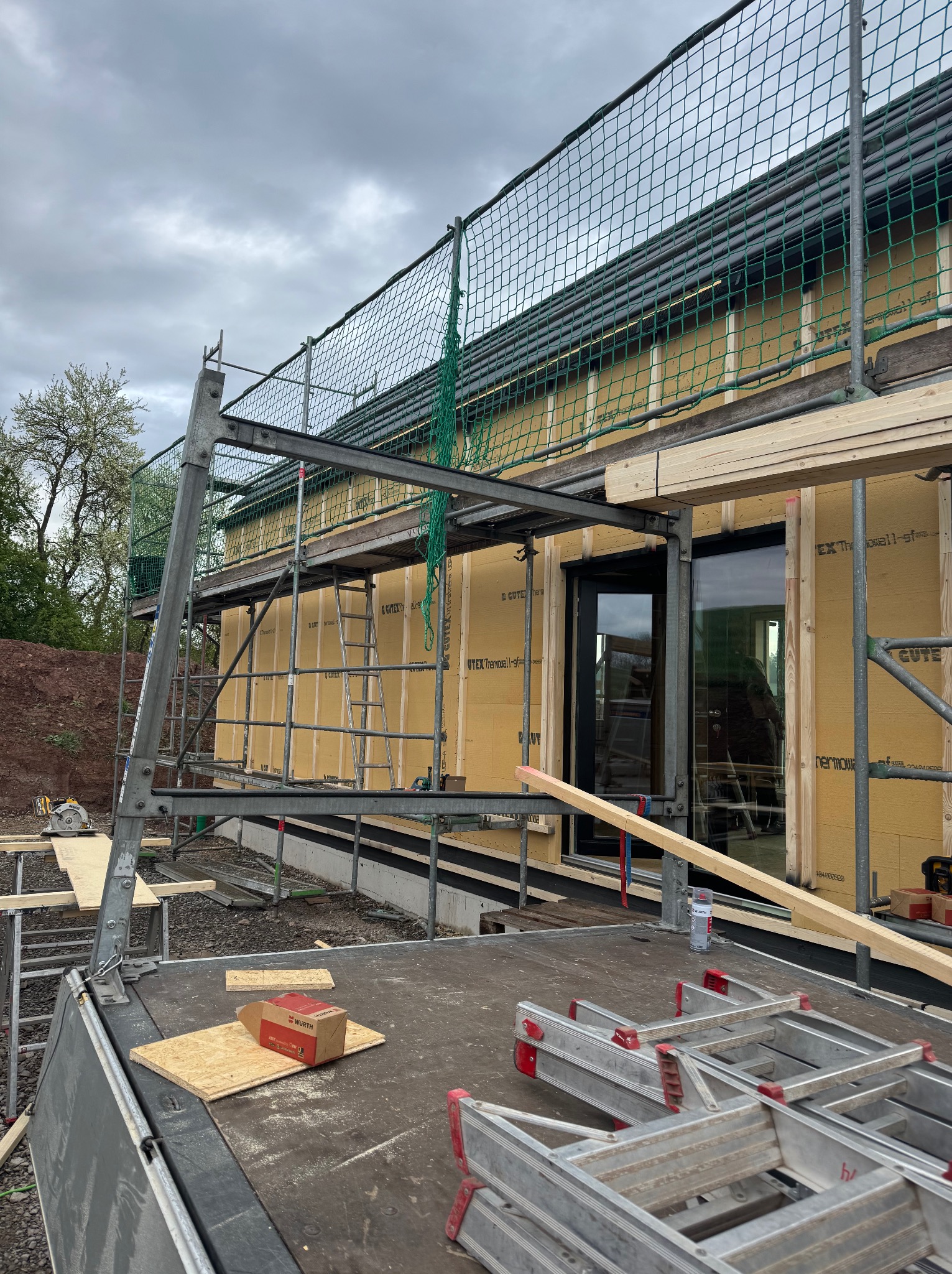 Budowa domu w trakcie ocieplania ścian zewnętrznych, widoczne rusztowania, płyty izolacyjne GUTEX i narzędzia. Dom jednorodzinny w stanie surowym otwartym.