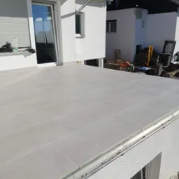 Jasnoszara, ceramiczna posadzka ułożona na tarasie domu jednorodzinnego, widok z g&oacute;ry na świeżo wykończoną powierzchnię z widocznym systemem odprowadzania wody.