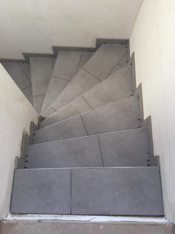 Schody wyłożone szarymi płytkami ceramicznymi z metalowymi listwami krawędziowymi, widok z góry na zakręt schodów.