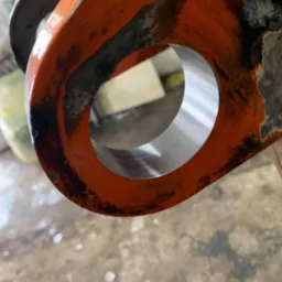 Precyzyjnie wytoczony otwór w pomarańczowym elemencie metalowym, widoczne ślady obróbki, surowe wykończenie zewnętrzne. Detal z bliska.