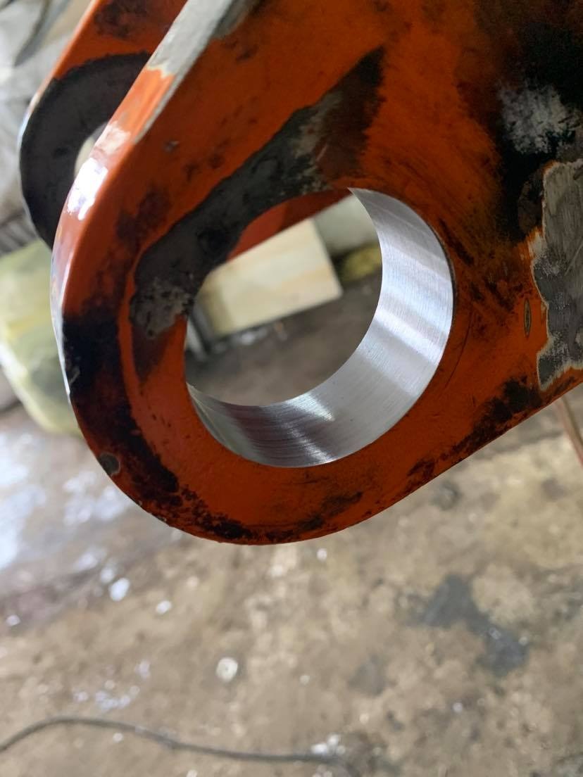 Precyzyjnie wytoczony otwór w pomarańczowym elemencie metalowym, widoczne ślady obróbki, surowe wykończenie zewnętrzne. Detal z bliska.