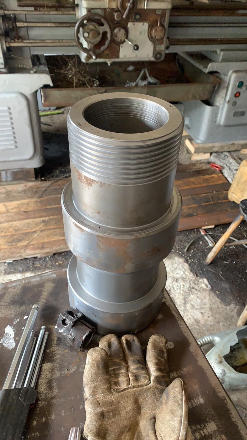 Obrabiany, stalowy element z gwintem na tokarce. Na stole leżą klucze imbusowe i robocza rękawica, co sugeruje etap pracy.