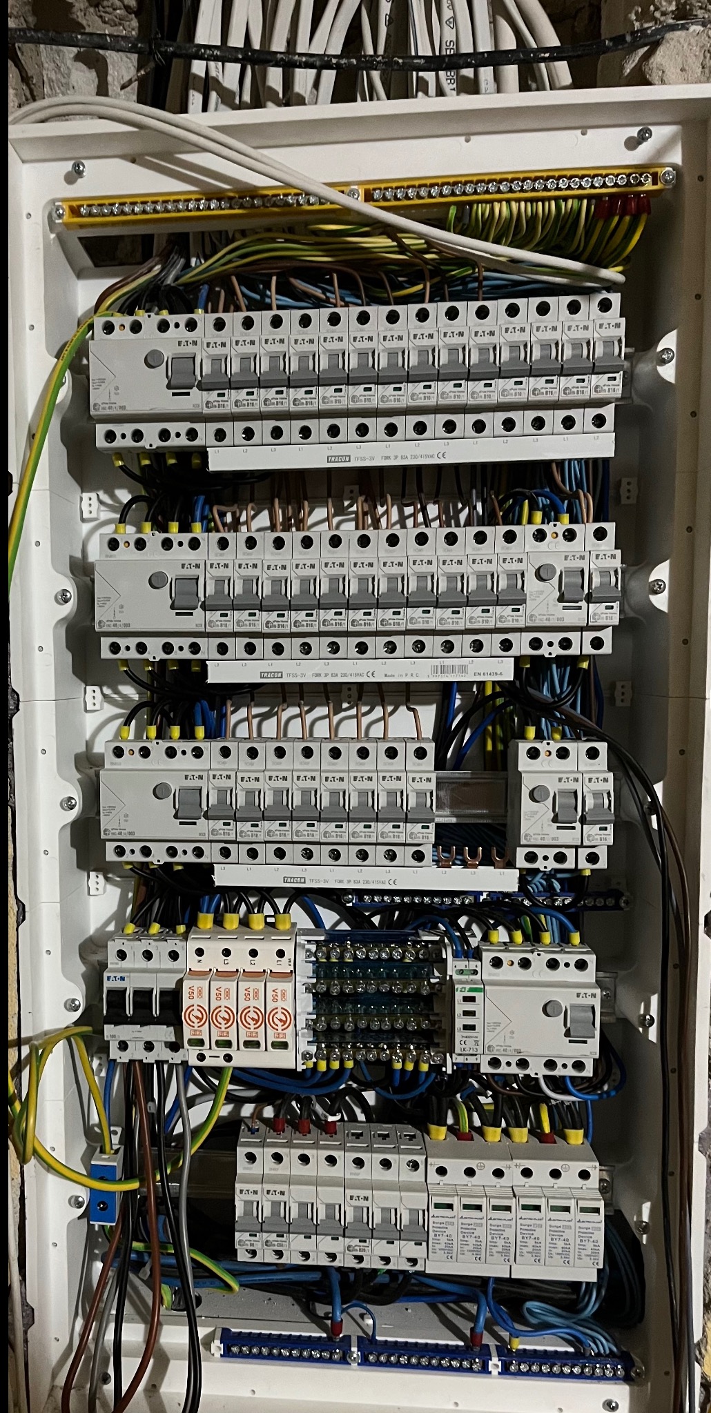 Rozdzielnica elektryczna z zamontowanymi bezpiecznikami i okablowaniem w białej obudowie, widok z bliska na instalację wewnątrz skrzynki.