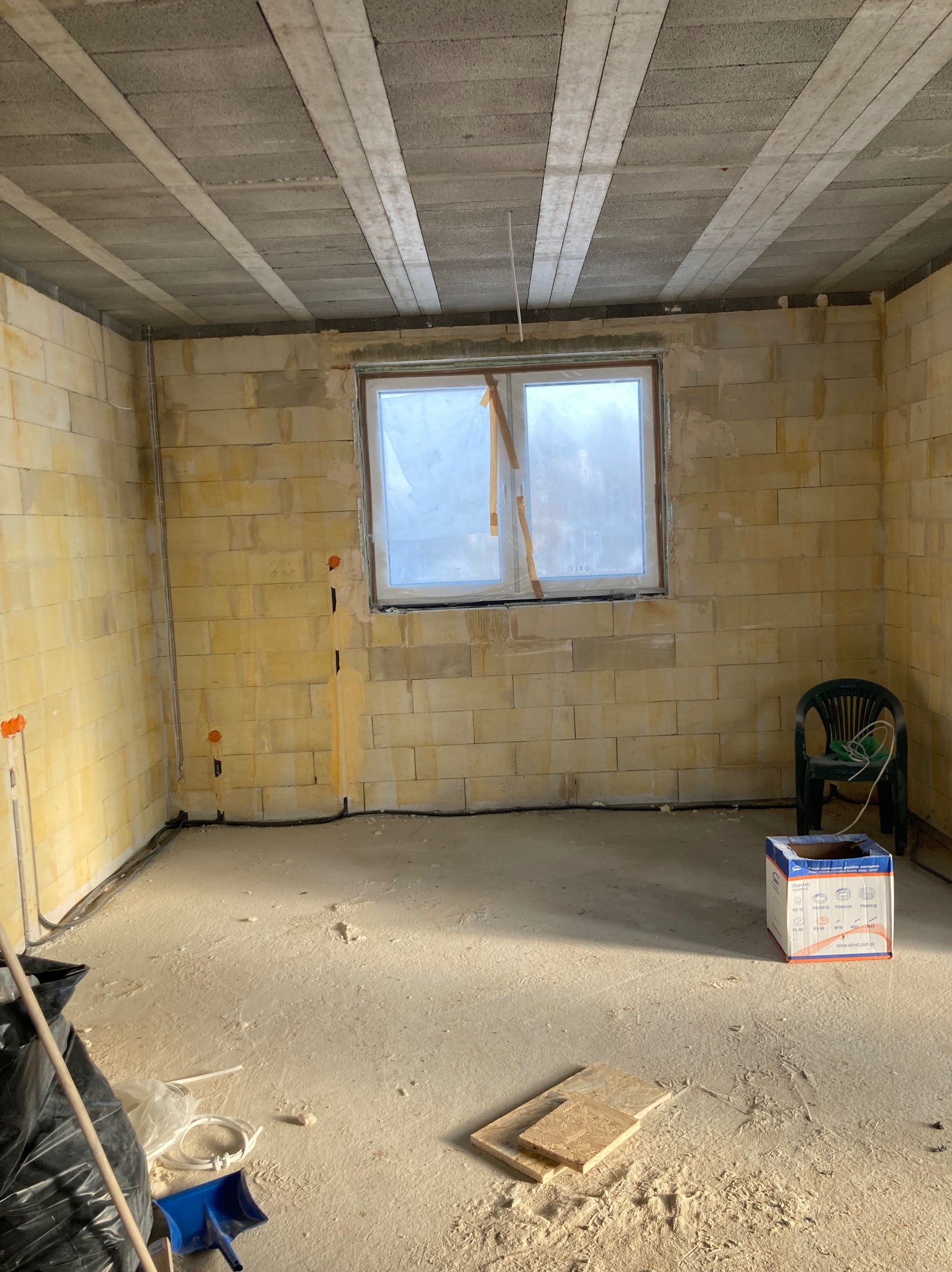 Surowy stan wnętrza z widocznymi przewodami elektrycznymi w ścianach z pustaków, przygotowany do dalszych prac wykończeniowych.