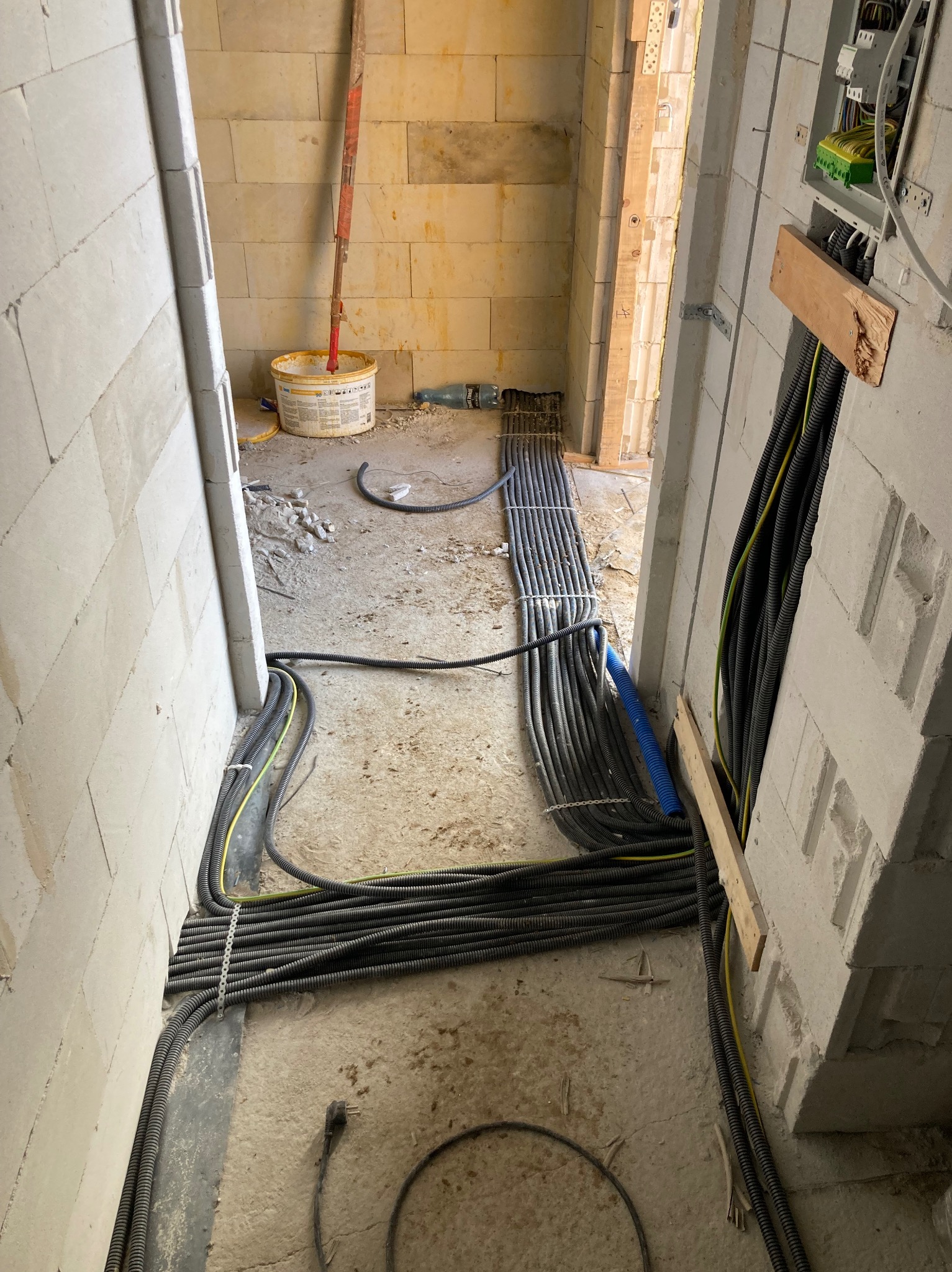 Wnętrze w trakcie prac elektrycznych: liczne kable w peszlach ułożone wzdłuż ścian, prowadzące do rozdzielni, widoczne narzędzia i materiały budowlane w tle.