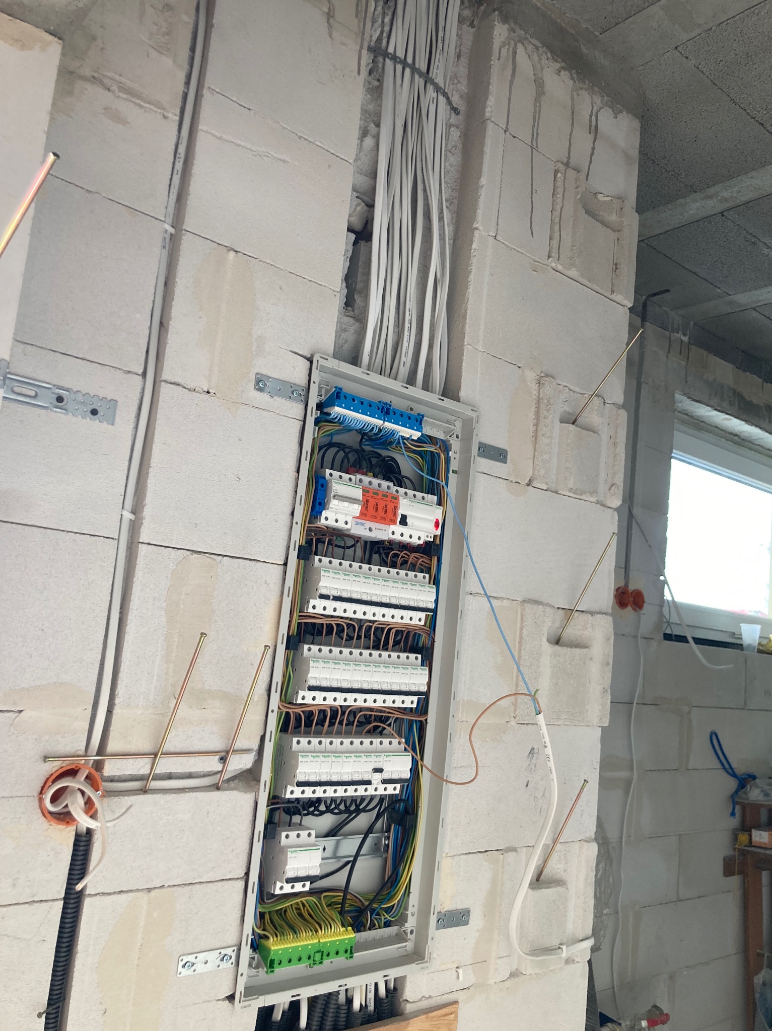 Rozdzielnia elektryczna z przewodami w surowym wnętrzu, widoczne zabezpieczenia i okablowanie. Ściany z betonu komórkowego, instalacja w trakcie montażu.