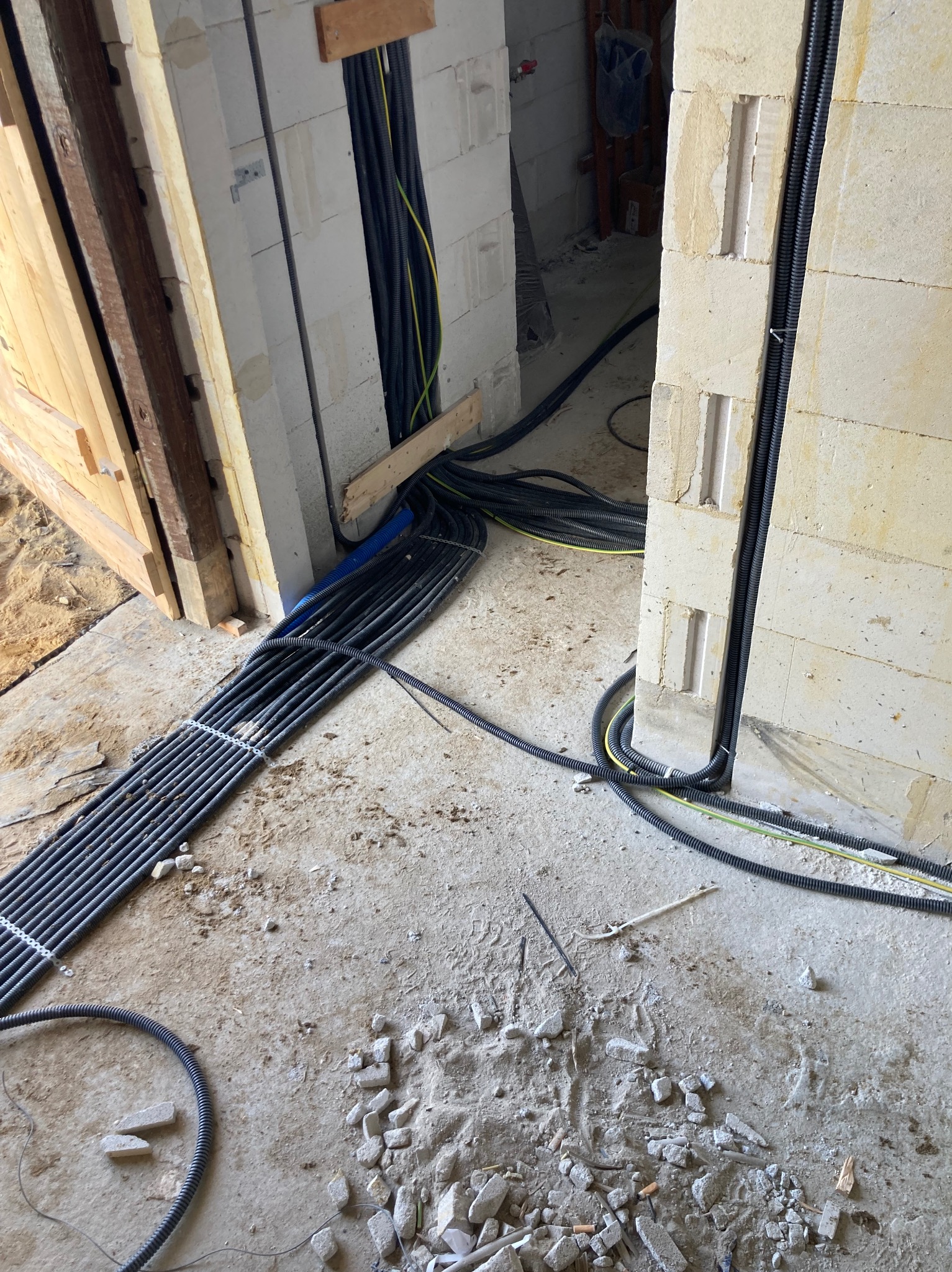 Kable elektryczne w peszlach prowadzone w ścianie z betonu komórkowego. W tle widoczne kolejne przewody. Etap prac instalacyjnych w surowym budynku.