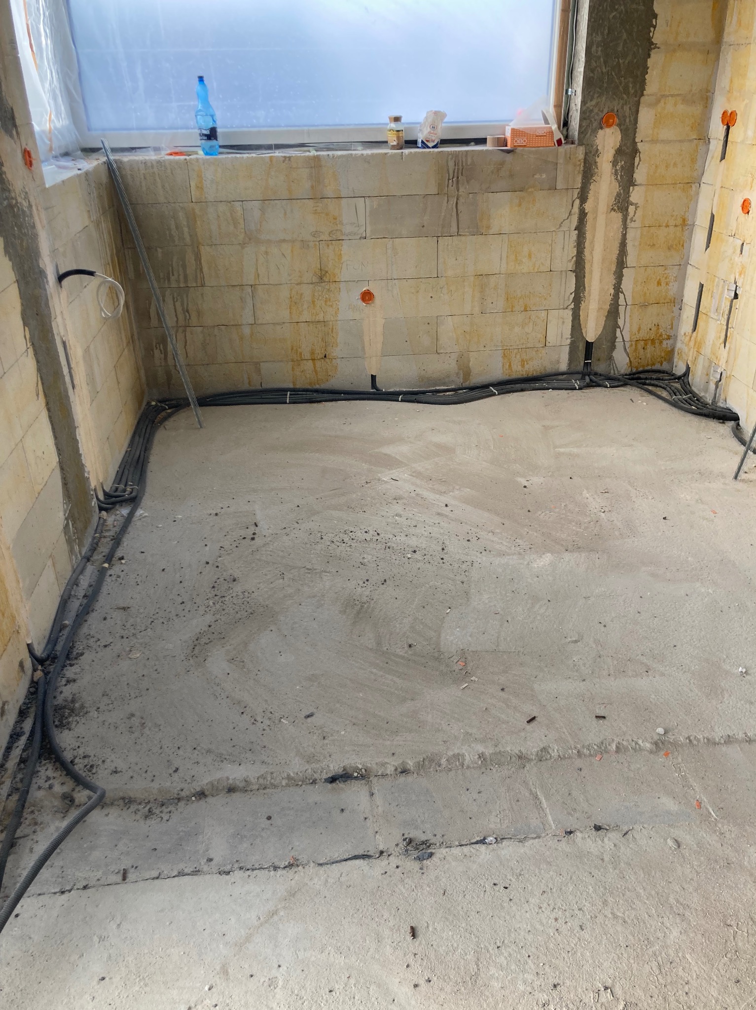 Surowy stan wnętrza z widocznymi przewodami elektrycznymi ułożonymi wzdłuż ścian, przygotowany do dalszych prac wykończeniowych. Widoczne puszki instalacyjne w ścianach.