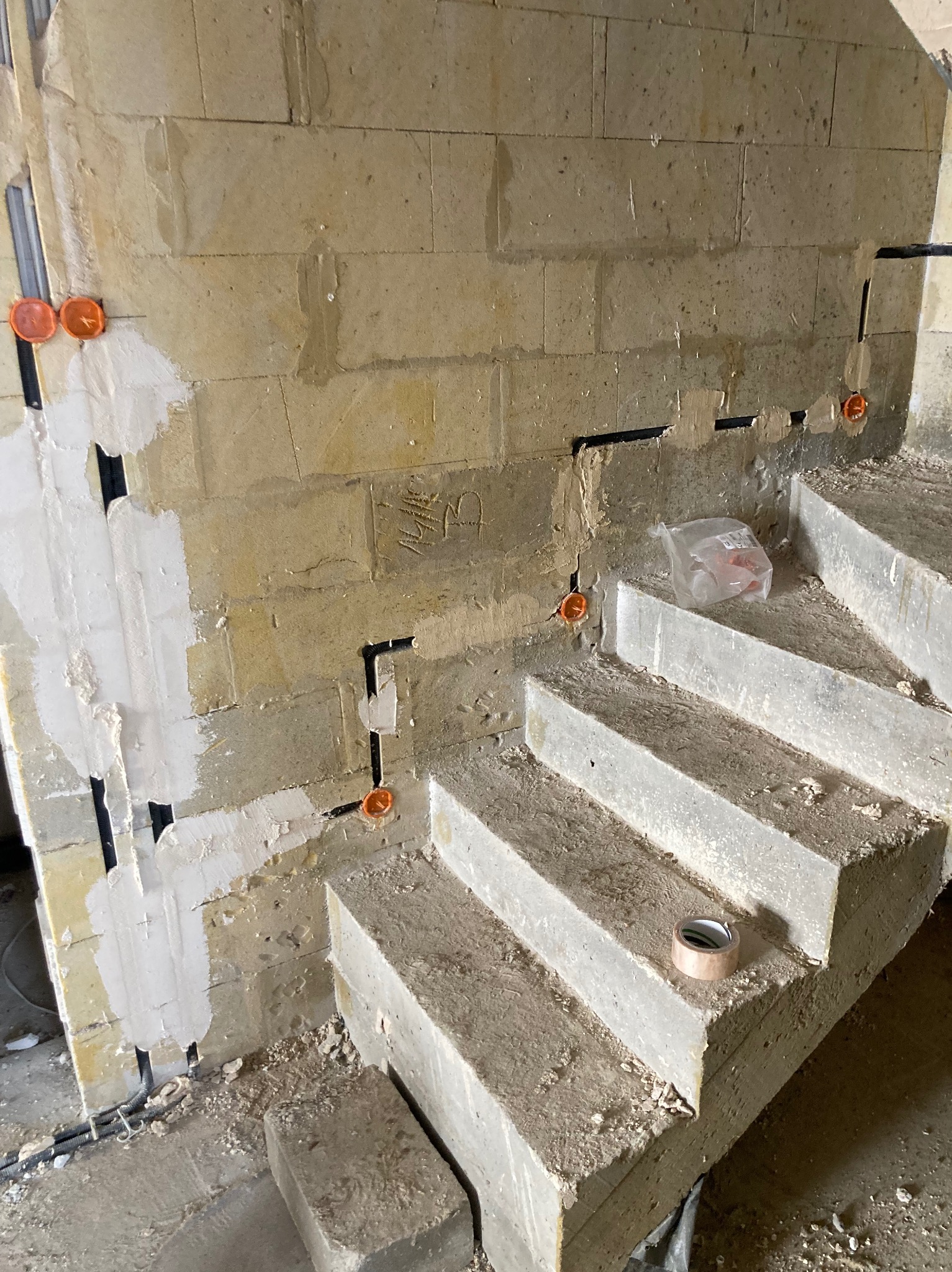 Surowe ściany z widoczną instalacją elektryczną w peszlach i puszkami, fragment betonowych schodów. Widoczne ślady prac murarskich i elektrycznych.