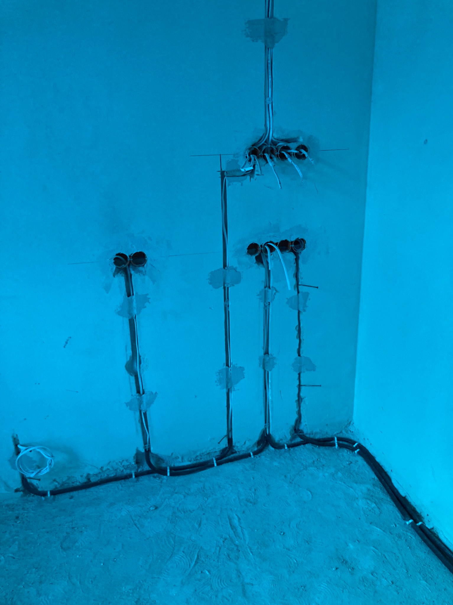 Rozprowadzone kable elektryczne w ścianie, widoczne puszki instalacyjne i przewody. Instalacja w surowym stanie, przed tynkowaniem.