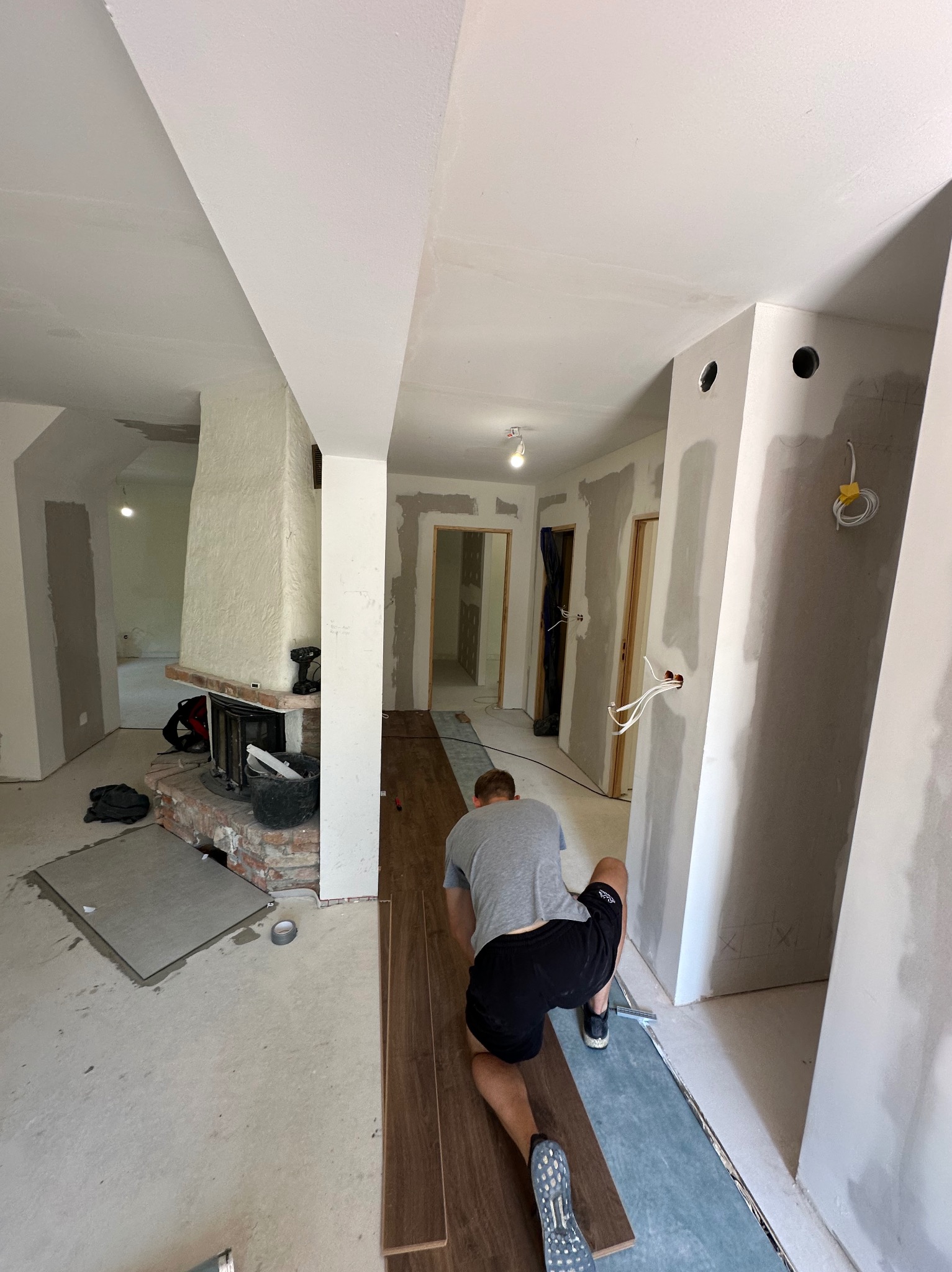 Układanie paneli podłogowych w trakcie remontu pokoju z kominkiem. Widoczne przygotowane podłoże, panele i narzędzia. Praca w toku.