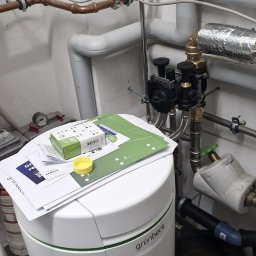 FABIOTECH Roman Pyrdoł - Kompleksowa instalacja wodno-grzewcza z białym systemem uzdatniania wody Grünbeck, miedzianymi rurami, pompami i licznikiem gazu w pomieszczeniu technicznym.