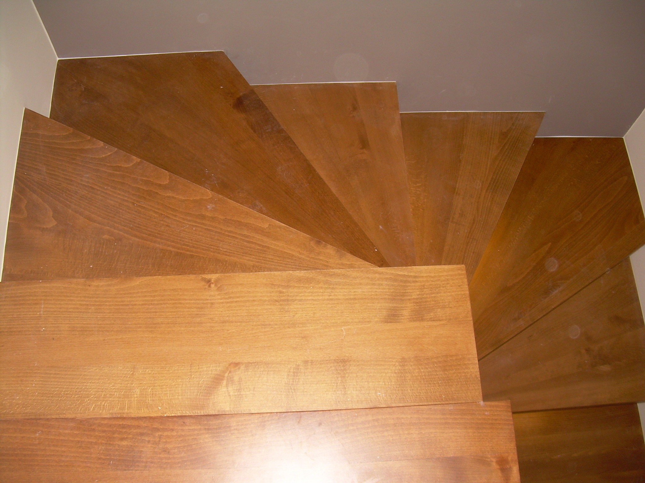 Ujęcie z góry na drewniane schody o ciepłym odcieniu, z widoczną fakturą drewna i detalami konstrukcyjnymi, prowadzące w górę wzdłuż ściany.