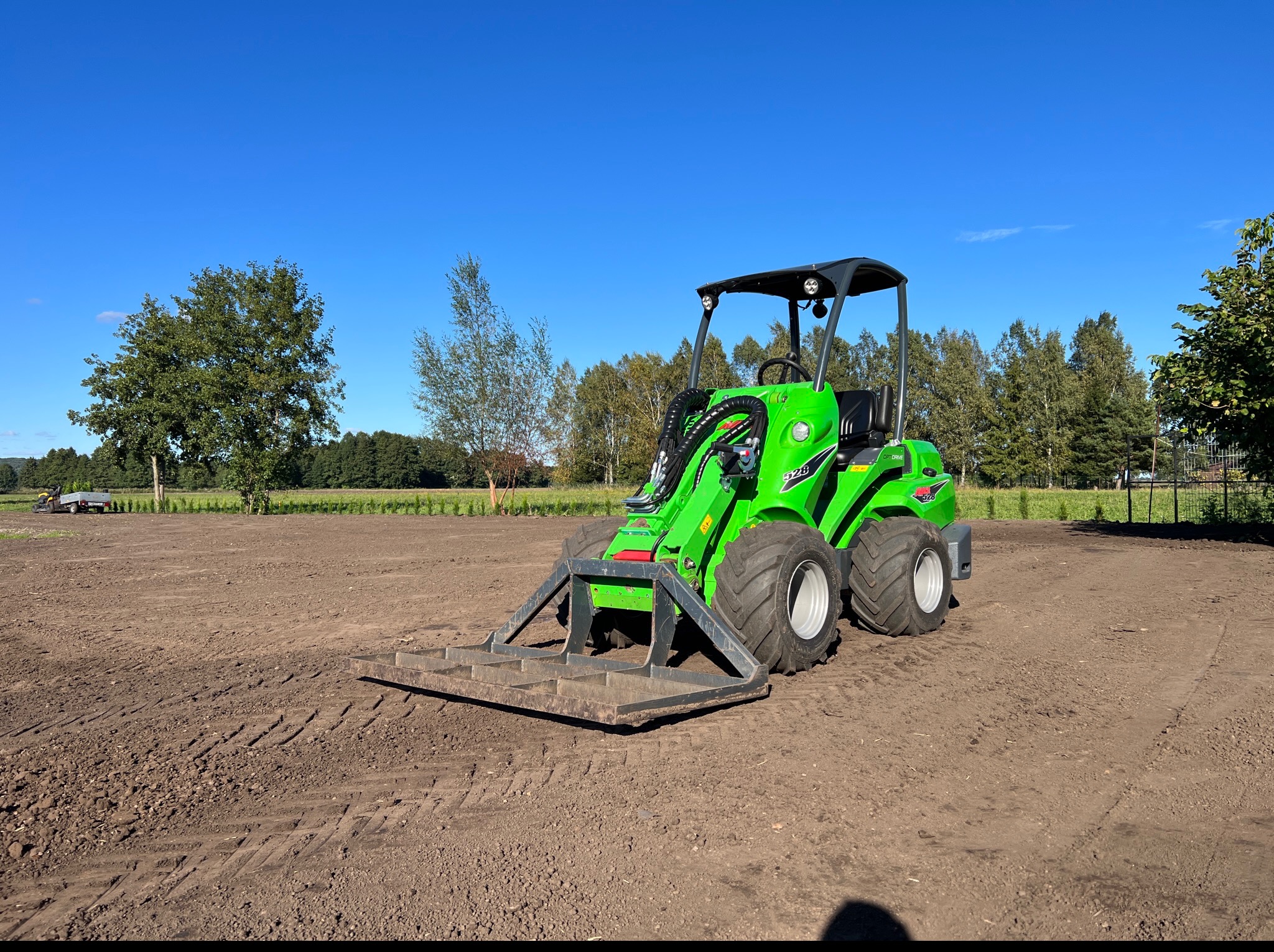 Zielony miniładowarka Avant 528 z równiarką na przygotowanym terenie w Pyrzanach, błękitne niebo w tle. Sprzęt do niwelacji.