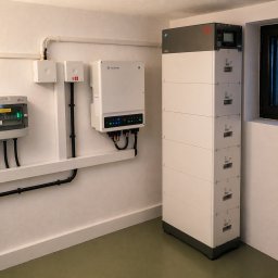 UniEnergy - Kompletna instalacja: falownik GoodWe, magazyn energii BYD 16,56 kWh i rozdzielnia elektryczna na ścianie w pomieszczeniu z oknem. Widoczne okablowanie.