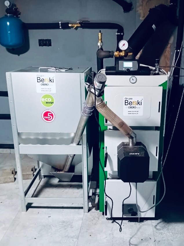 Nowoczesny, dwuczęściowy piec z podajnikiem, marki Berski Obero, z widocznym certyfikatem Eco Design i klasą 5, stojący w kotłowni.