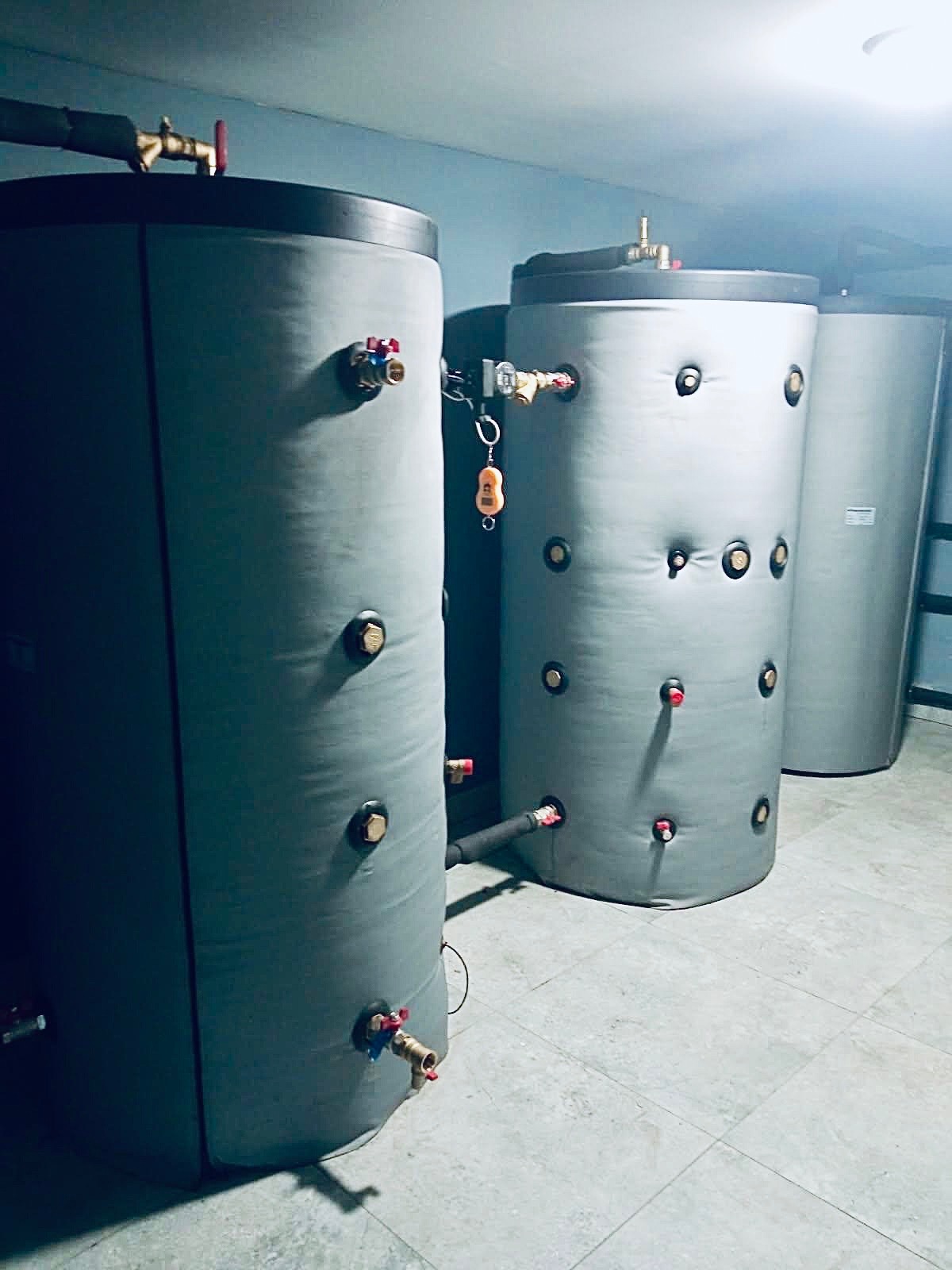Szare, ocieplone zbiorniki akumulacyjne na wodę w kotłowni, z widocznymi zaworami i przyłączami, zainstalowane w ramach systemu grzewczego.