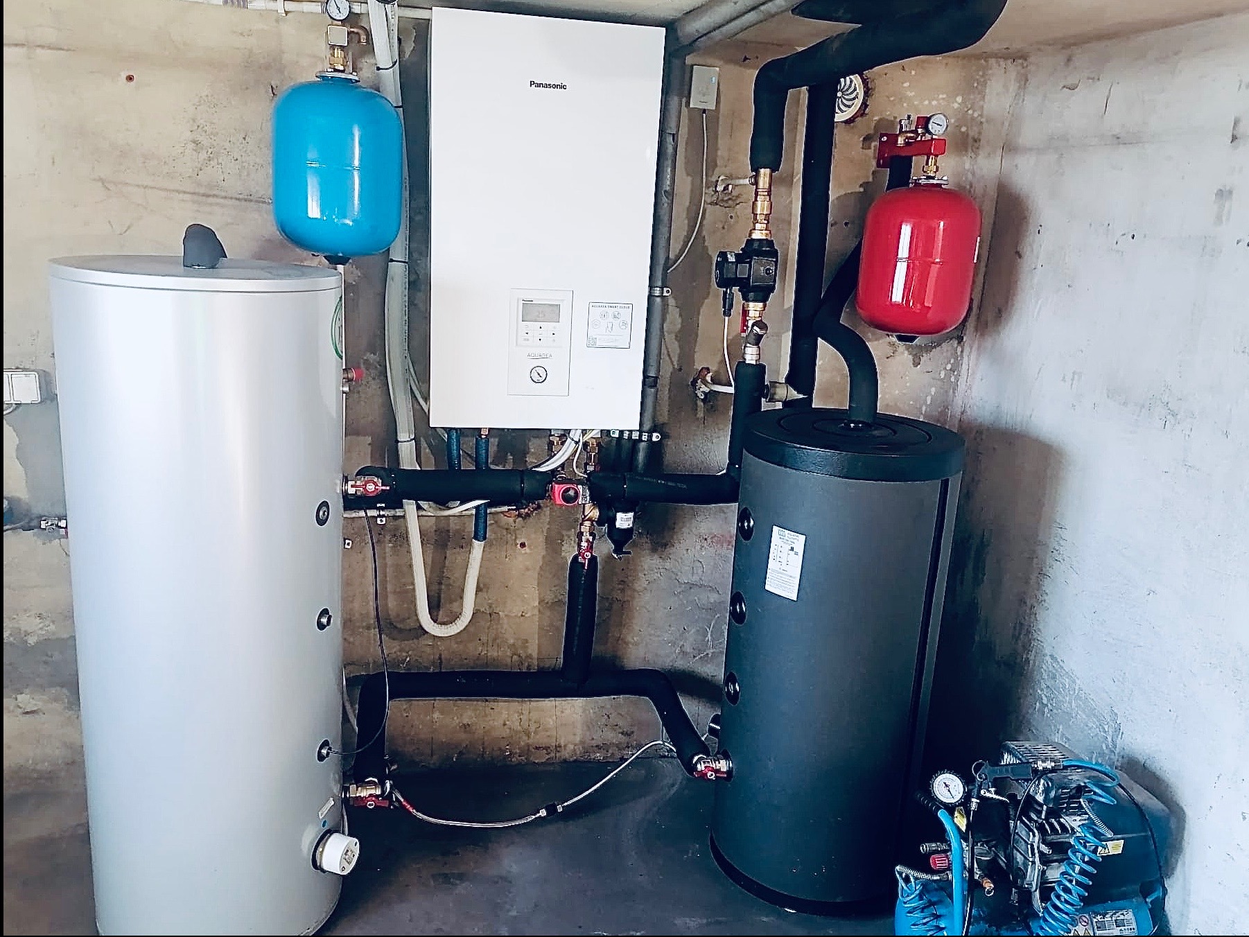 Instalacja C.O. z piecem Panasonic, zbiornikami: białym, niebieskim i czerwonym. Czarny zbiornik ciepłej wody użytkowej. Elementy instalacji w kotłowni.