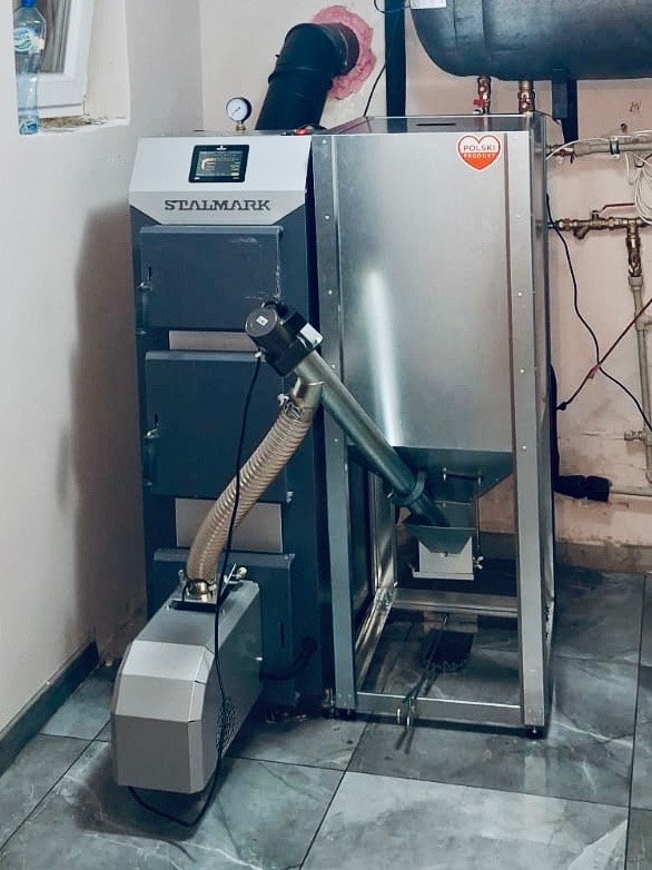 Kotłownia z piecem Stalmark na ekogroszek, z podajnikiem ślimakowym i zasobnikiem. Widoczne elementy instalacji grzewczej.