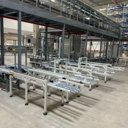 MSL POWER SPÓŁKA Z OGRANICZONĄ ODPOWIEDZIALNOŚCIĄ - Wnętrze hali magazynowej z systemem transportu rolkowego na dwóch poziomach. Metalowa konstrukcja wsporcza, białe rolki transportowe, szara betonowa posadzka.