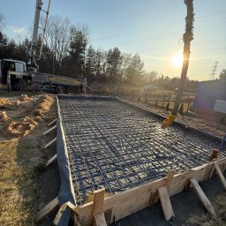 Sinaj Serhii Lylyk - Zbrojenie fundamentów z szalunkiem i pompą do betonu w tle, oświetlone promieniami zachodzącego słońca. Widok na przygotowany teren pod wylewkę.