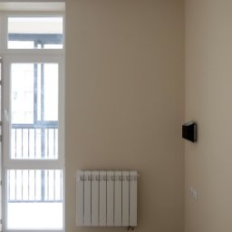 M&K - Jasne wnętrze po remoncie: beżowe ściany, biały grzejnik pod oknem balkonowym, drewnopodobna podłoga. Minimalistyczny design, czysty kadr.