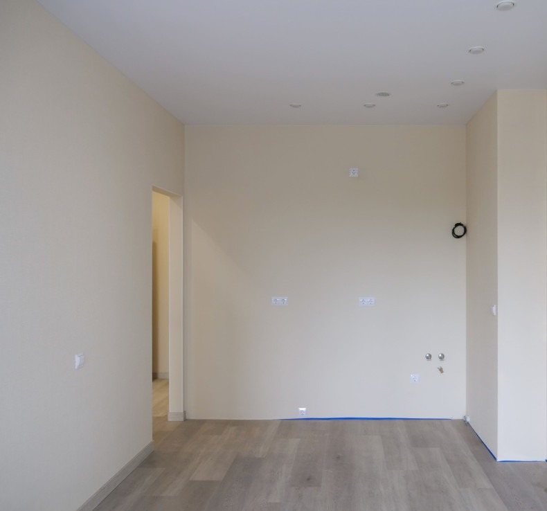 Jasne, świeżo pomalowane wnętrze z drewnianą podłogą i przygotowanymi instalacjami. Widoczne punkty świetlne i gniazdka elektryczne, gotowe do dalszego wykończenia.