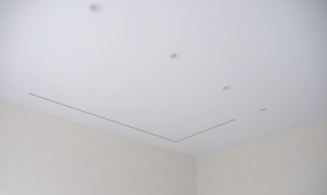 Biały sufit z wpuszczonymi lampami LED i minimalistycznym wzorem w kształcie litery L, widok z narożnika pokoju.