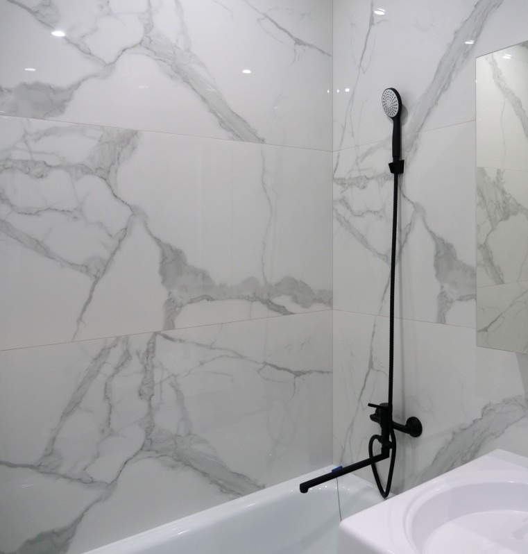 Biała łazienka z marmurowymi płytkami, czarna armatura. Nowoczesny design, widok na wannę i umywalkę. Minimalistyczne wykończenie.