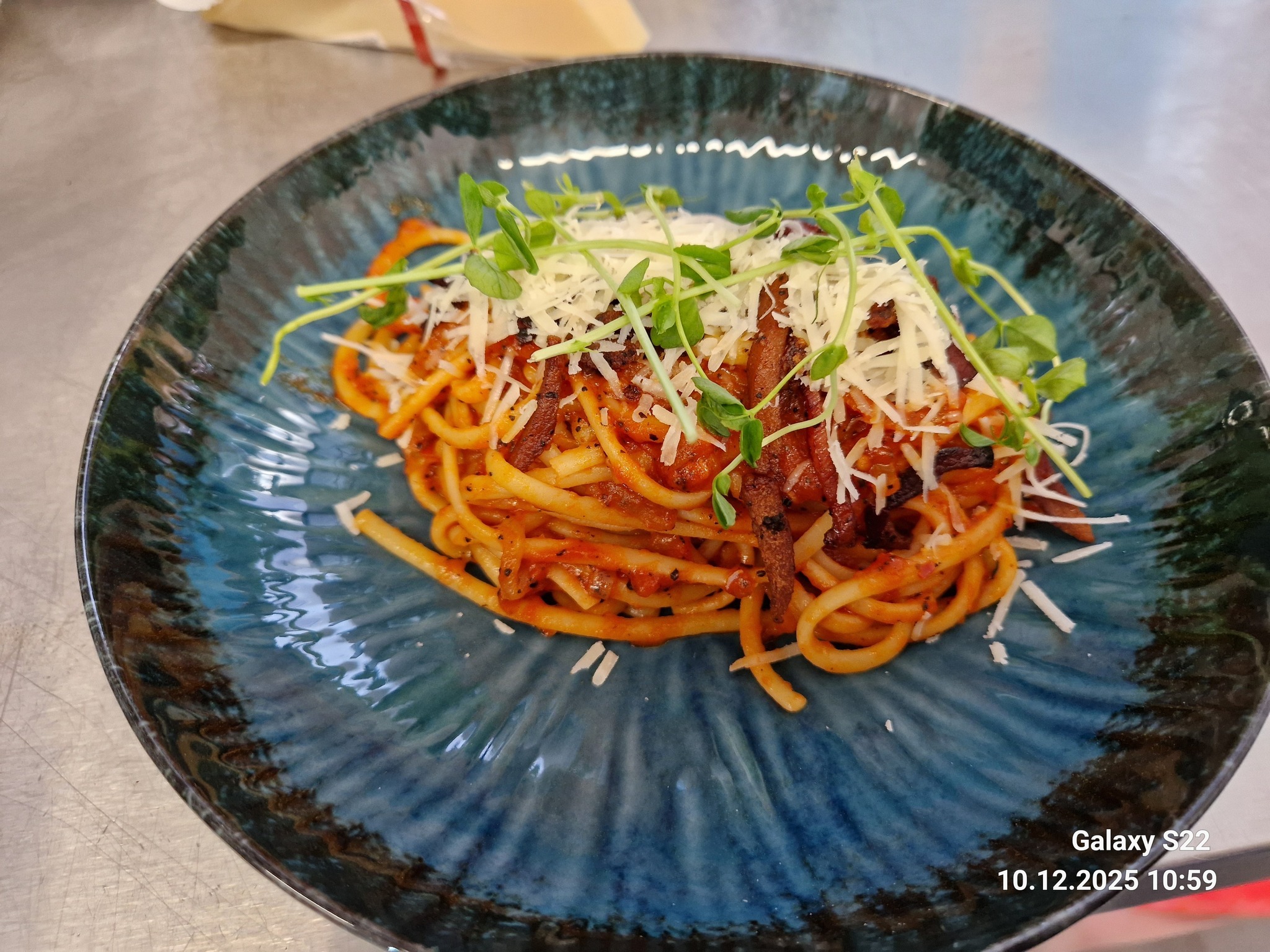 Apetyczne spaghetti z sosem pomidorowym, boczkiem, serem i świeżymi kiełkami na talerzu w odcieniach błękitu i brązu. Danie gotowe do spożycia.