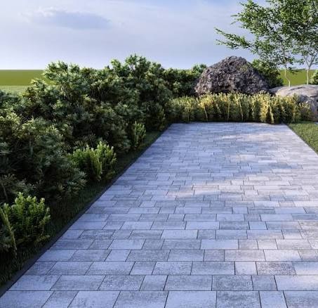 Ułożona, szara kostka brukowa w ogrodzie, otoczona zielenią. Widok z góry, prezentujący wzór ułożenia i estetyczne wykończenie ścieżki ogrodowej.