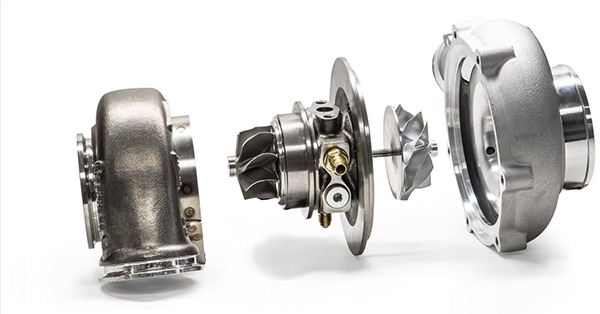 Rozłożona turbosprężarka samochodowa na białym tle, ukazująca wirniki i obudowy, co sugeruje naprawę lub tuning silnika.